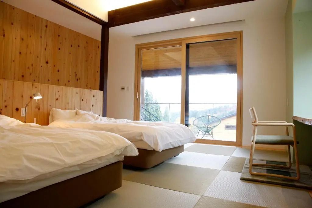 Helles Schlafzimmer mit zwei Betten und Balkonzugang im Satoyama Jujo Hotel