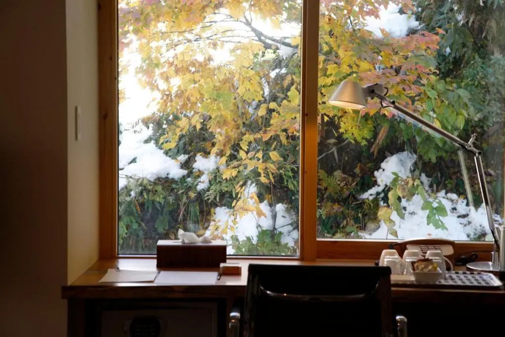 Gemütlicher Schreibtisch mit Blick auf herbstliche Bäume und Schnee
