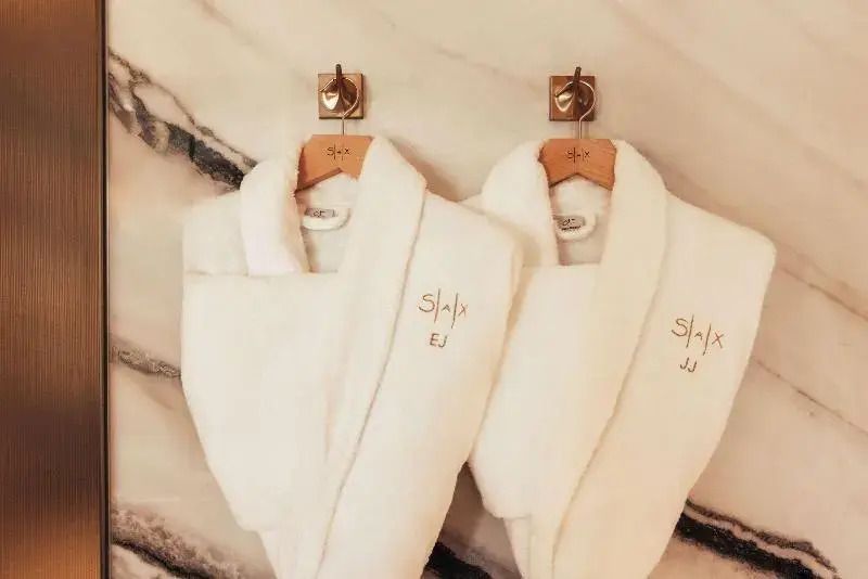 Zwei flauschige Bademäntel mit gesticktem Logo auf einer marmorierten Wand.