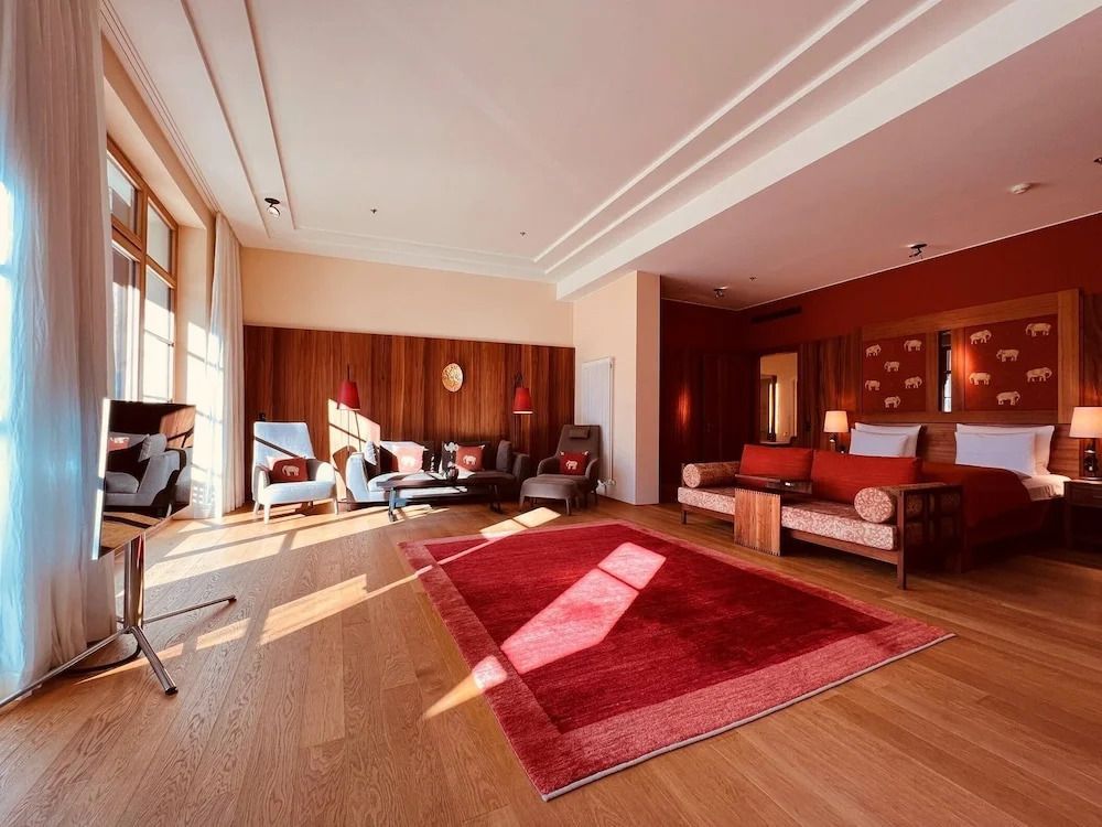 Geräumiges Zimmer mit Holzverkleidung und roten Akzenten. Großes Fenster mit Tageslicht.