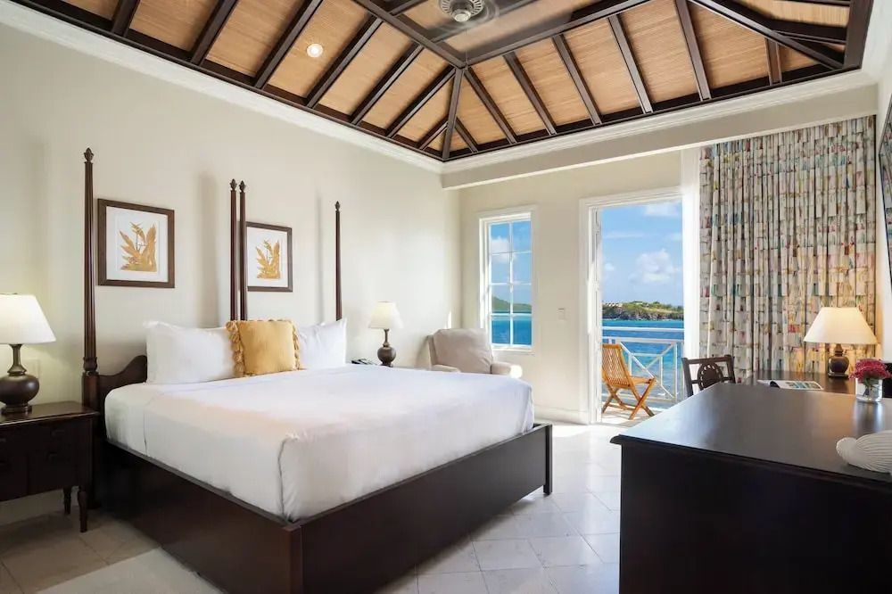 Helles Zimmer mit Doppelbett und offener Tür zum Balkon mit Meerblick