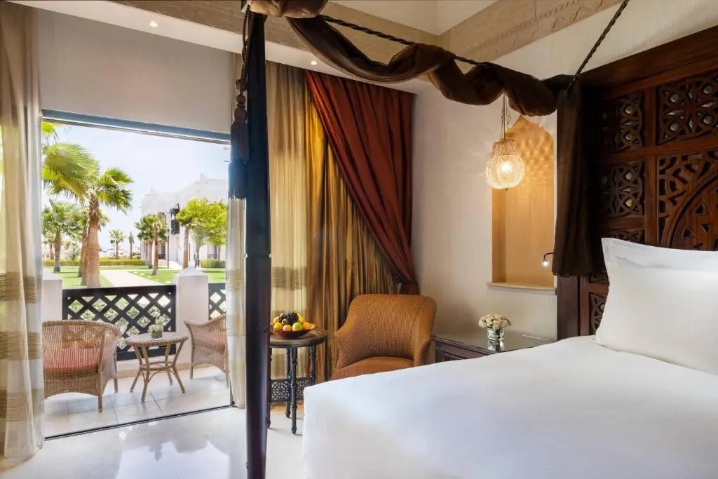 Seitlicher Blick aus dem Deluxe Doppelzimmer auf Sitzbereich und Garten im Sharq Village & Spa.