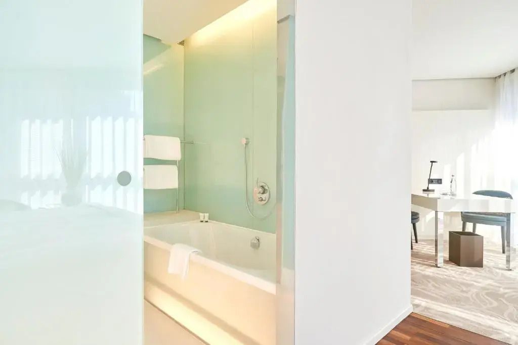 Badezimmer mit Badewanne, gläserner Trennwand und heller Beleuchtung.