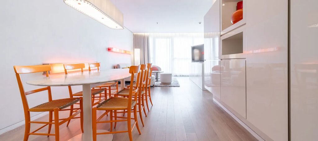 Helle Suite mit Esstisch und orangefarbenen Stühlen, modern eingerichtet.