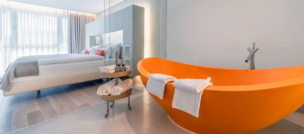 Freistehende orangefarbene Badewanne mit Handtüchern und Badutensilien.