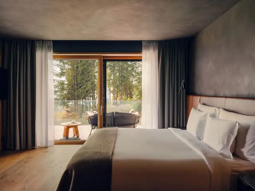 Gemütliches Schlafzimmer mit Doppelbett und Zugang zu einem möblierten Balkon mit Blick auf den Wald.