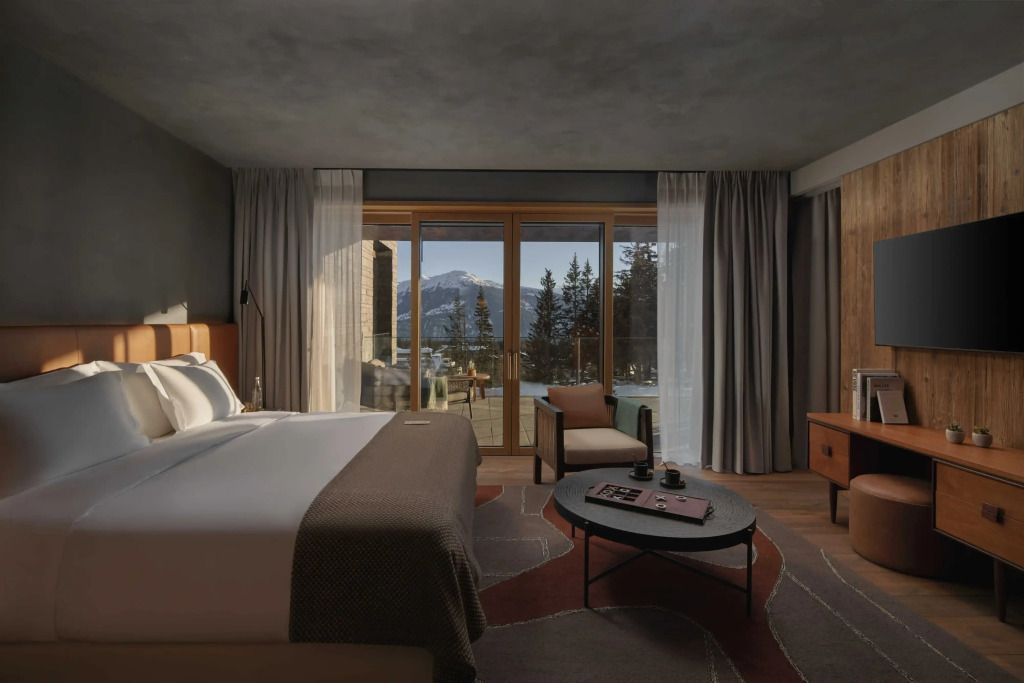 Geräumiges Zimmer mit Balkon und Doppelbett, Ausblick auf verschneite Berge.
