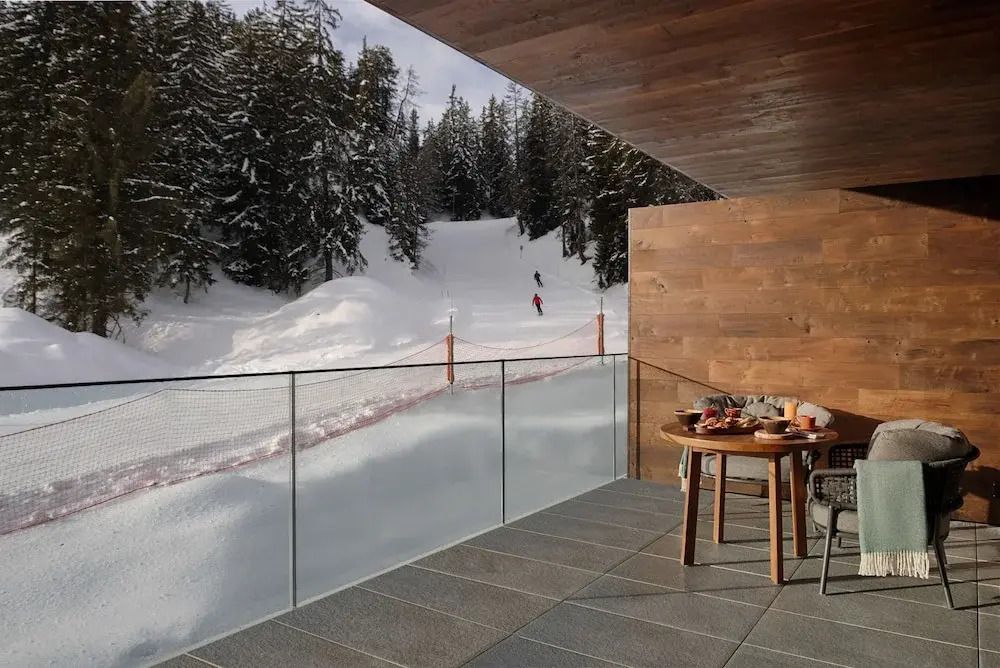 Balkon im Winter mit Blick auf verschneite Pisten und Tannenbäume