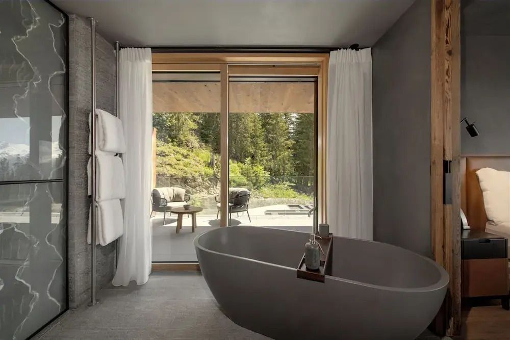 Edles Bad mit freistehender Wanne und großer Fensterfront mit Waldsicht