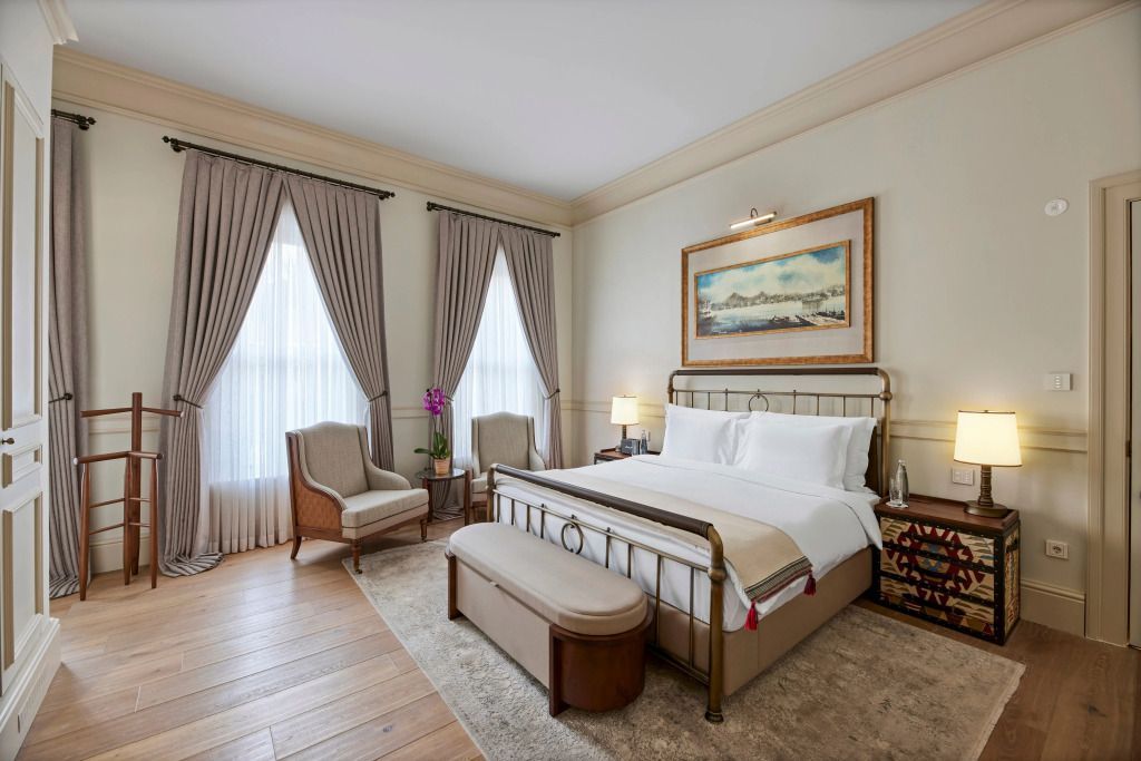 Elegantes Deluxe Doppelzimmer mit großen Fenstern, Doppelbett und Sitzgruppe.