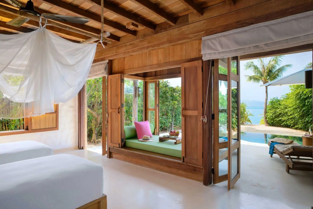 Offene Holzfenster mit Blick auf Terrasse, grünes Sofa und Meerblick