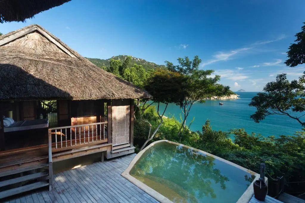 Villa mit Strohdach und Infinity-Pool, umgeben von üppiger Natur und Meerblick