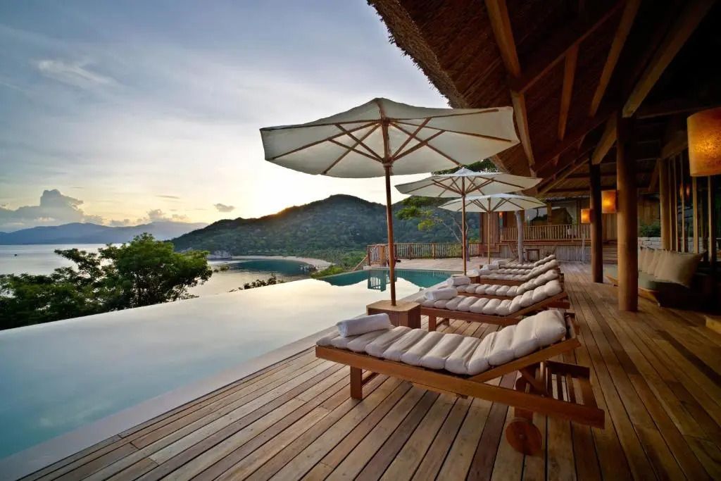 Infinity Pool mit Sonnenschirmen und Liegen vor Bergkulisse.