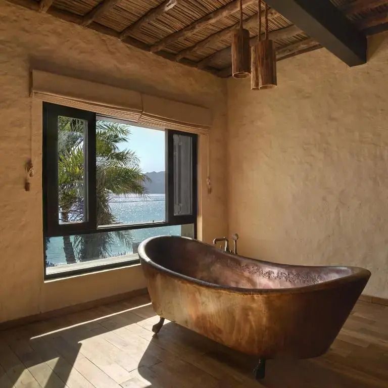 Freistehende Kupferbadewanne mit Blick aufs Meer durch ein großes Fenster