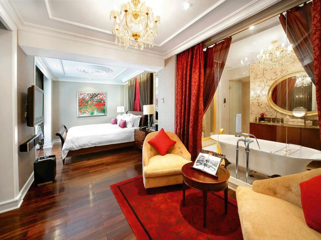 Luxuriöse Suite mit Doppelbett, eleganten Vorhängen und freistehender Badewanne.