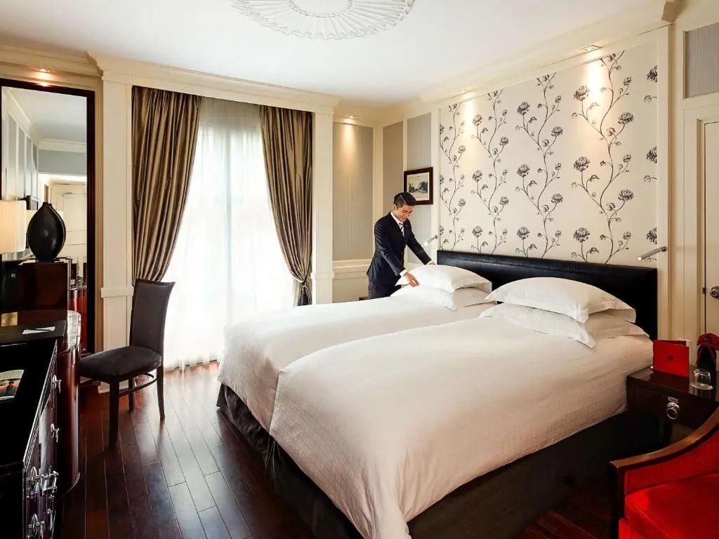 Elegantes Doppelzimmer im Sofitel Legend Metropole Hanoi mit stilvoller Tapete und Sitzbereich