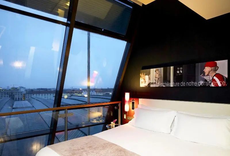 Junior-Suite mit Panoramafenster und Blick auf die Stadt bei Dämmerung.