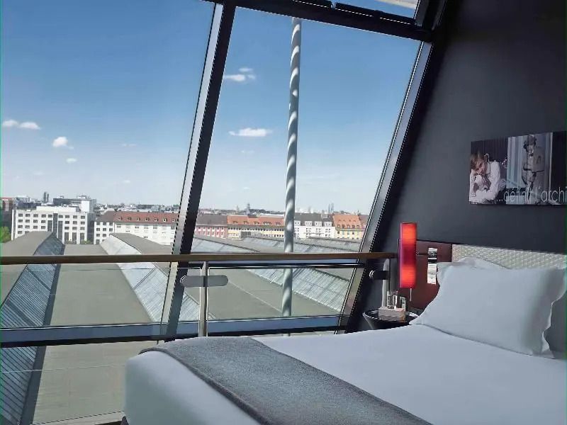 Schlafzimmer mit großem Fenster und Blick über die Dächer der Stadt an einem sonnigen Tag.