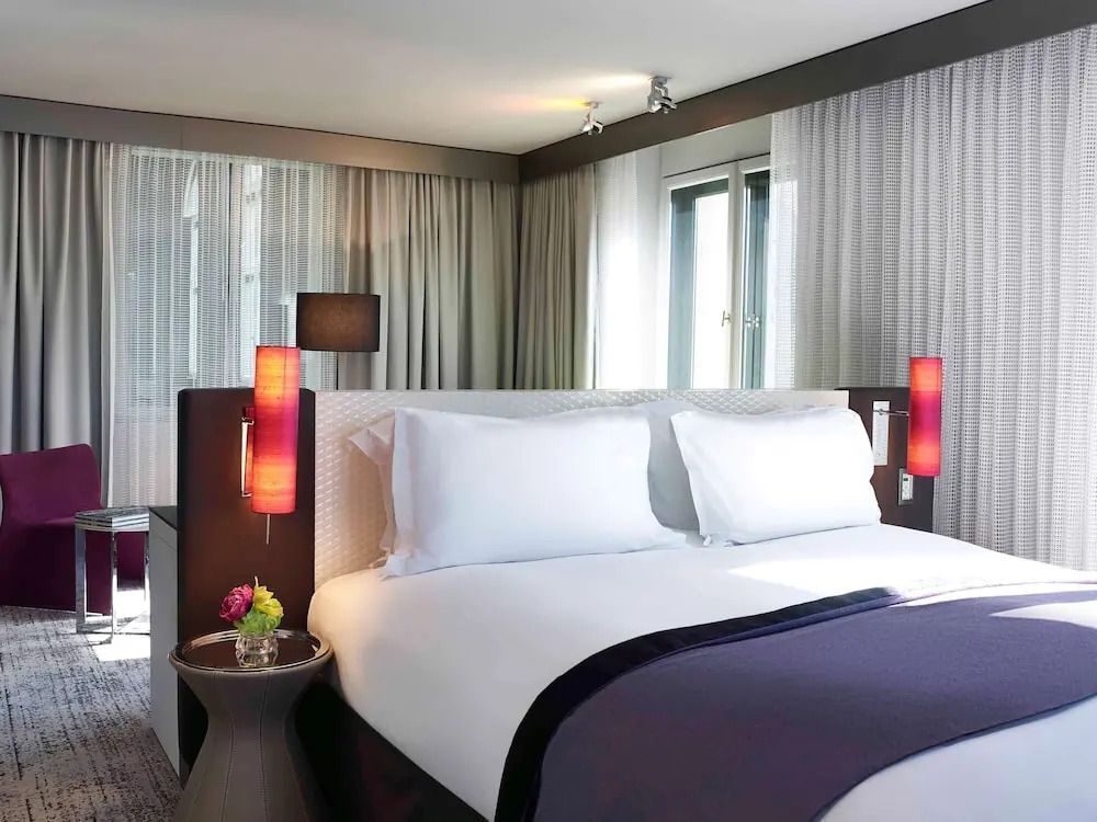 Einladendes Doppelbett mit stilvoller Beleuchtung in Junior-Suite des Sofitel Munich Bayerpost