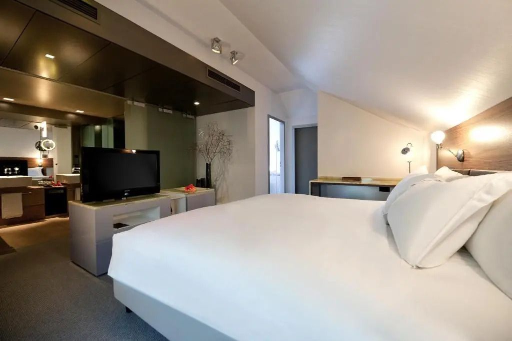 Helles Schlafzimmer mit Doppelbett und modernem TV in der Opera Suite