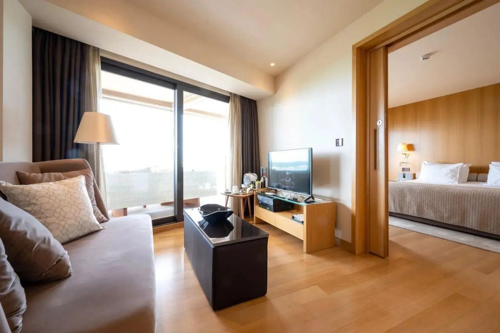 Helles Wohnzimmer mit Sofa, großem Fernseher und Zugang zum Balkon.