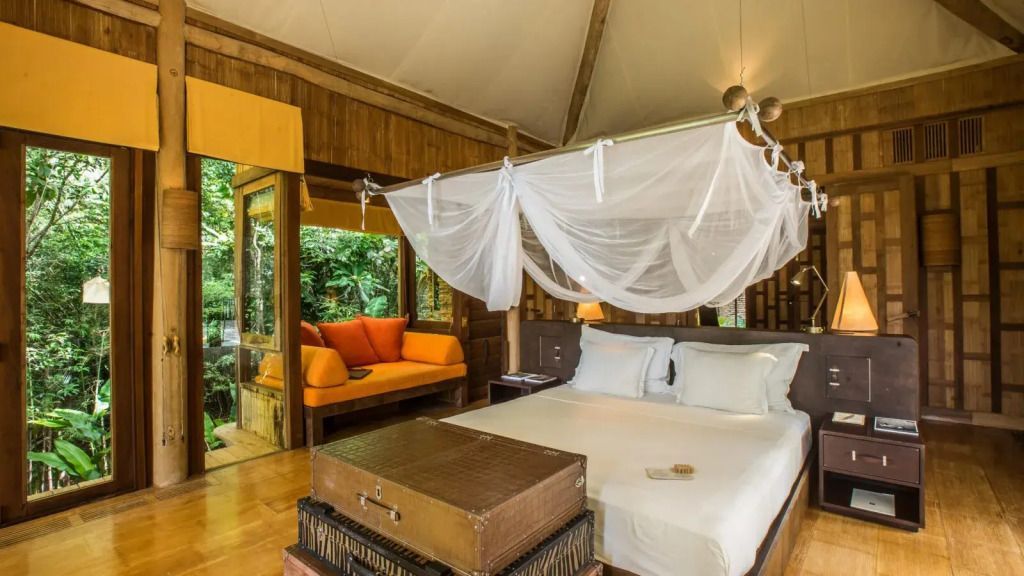 Helles Schlafzimmer mit Himmelbett und Sofaecke in tropischer Umgebung.