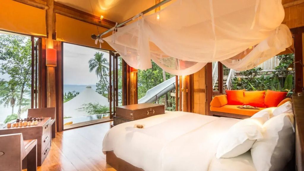 Luxuriöses Schlafzimmer mit Himmelbett und Blick auf tropischen Garten und Meer