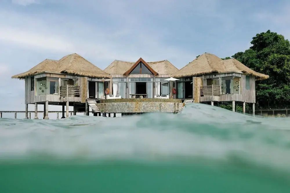 Luxusvilla auf Stelzen über klarem Wasser mit Strohdach und Terrasse