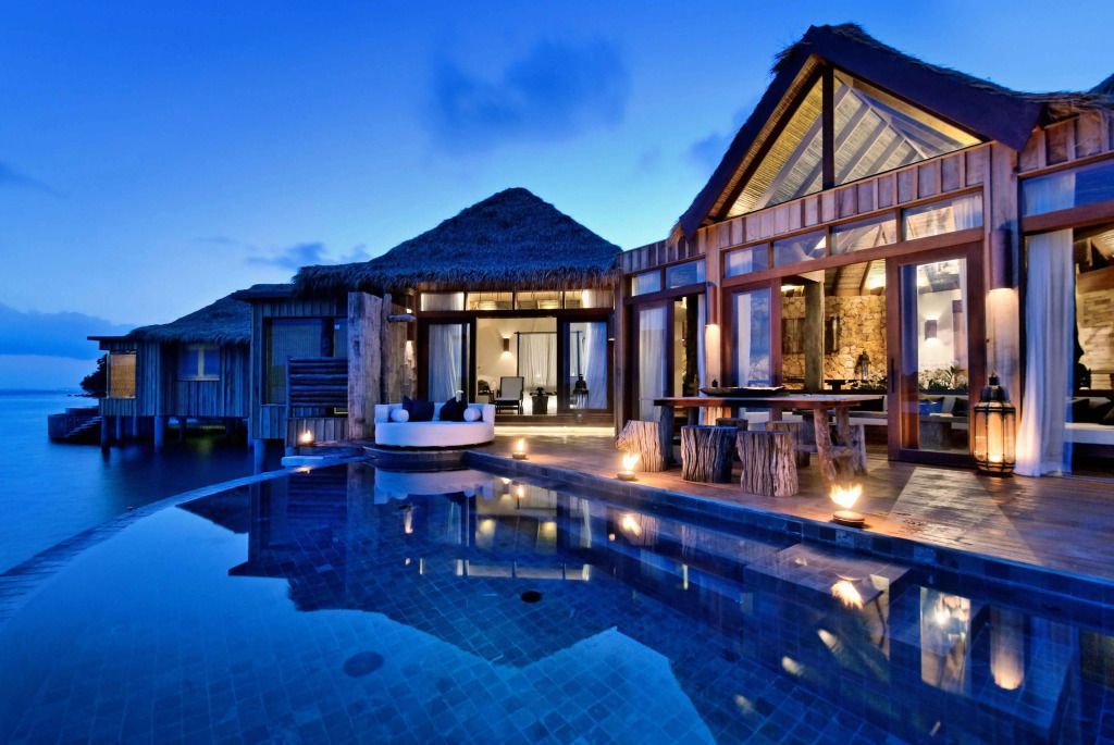 Beleuchteter Außenbereich der Villa bei Nacht mit Pool und Lounge.