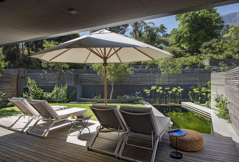 Terrasse mit Sonnenliegen und Sonnenschirm vor einem gepflegten Garten.