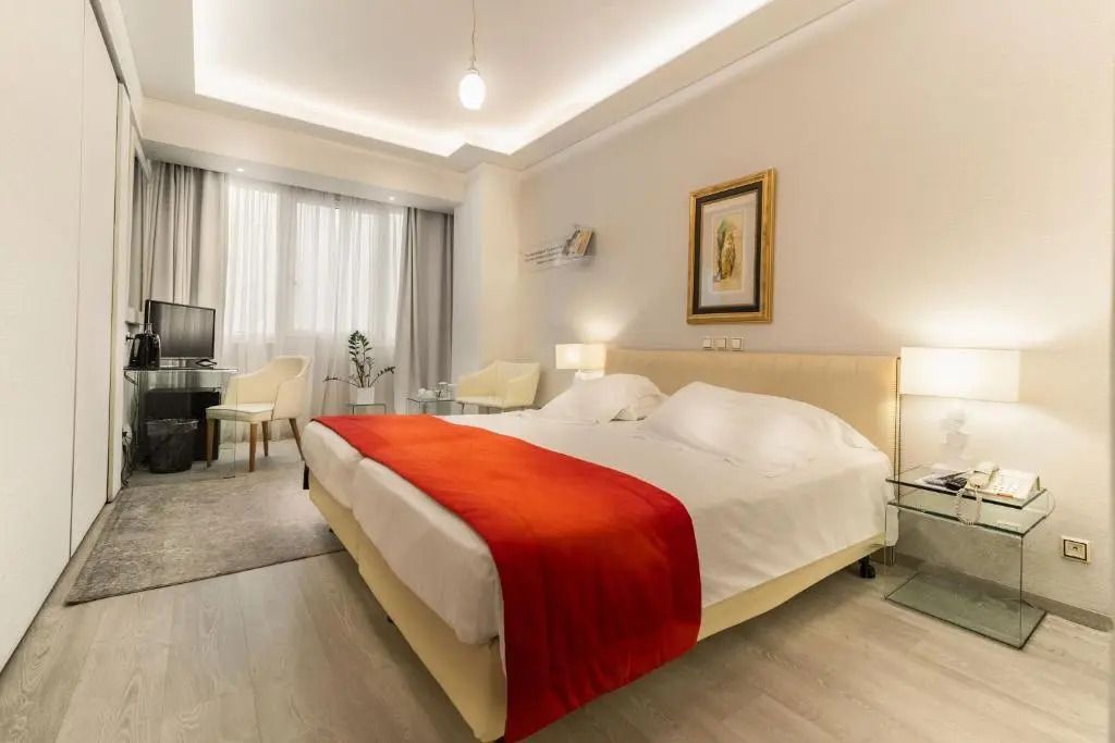 Dreier Zimmer mit elegantem rotem Bettüberwurf und gemütlicher Beleuchtung.