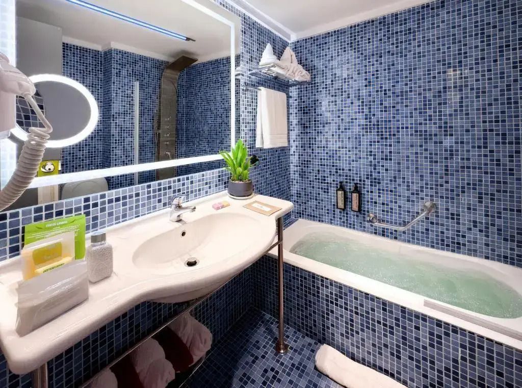 Badezimmer mit blauen Mosaikfliesen und beleuchtetem Spiegel