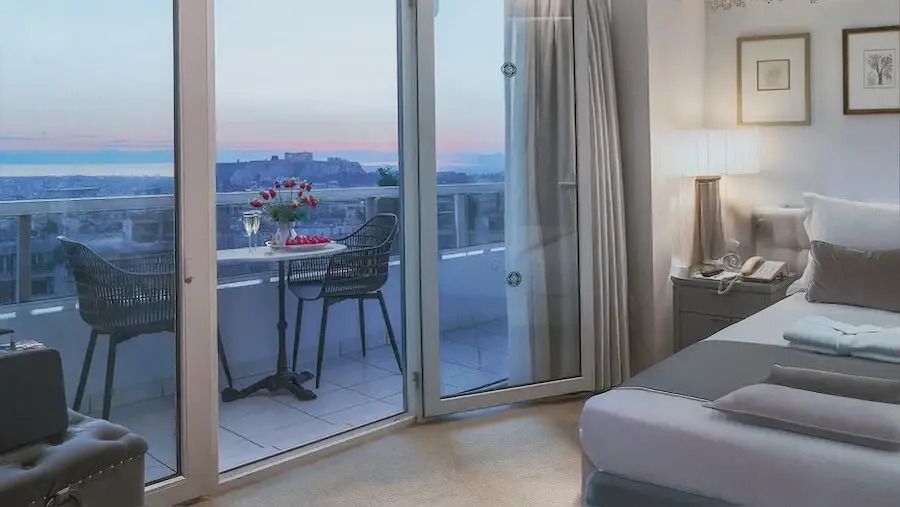 Zimmer mit offenem Balkon und Blick auf beleuchtete Akropolis bei Sonnenuntergang