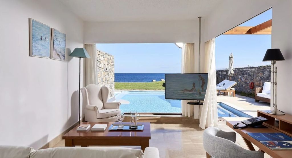 Geräumiger Wohnbereich mit Blick auf Pool und Meer. Elegante Möbel und großer Fernseher.