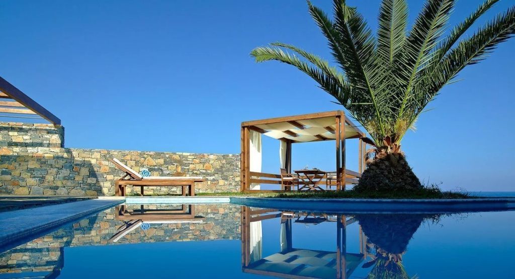 Pool mit Liegen und Pavillon umgeben von Palmen mit klarem Himmel