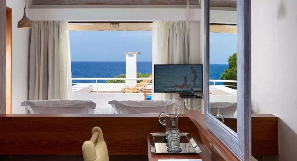 Helles Wohnzimmer mit Meerblick und TV, Terrasse mit Liegestühlen und blauem Himmel