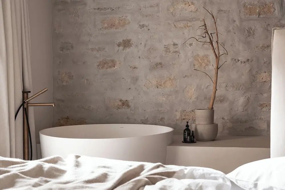 Ruhige Ecke mit Badewanne vor rustikaler Mauer und dekorativem Zweig