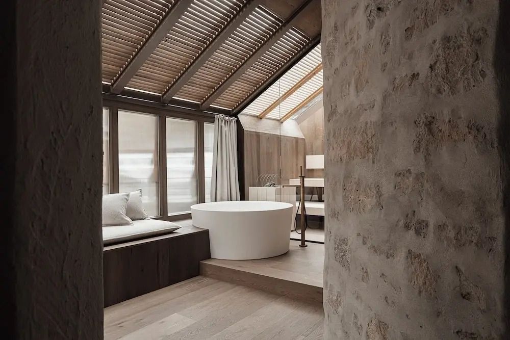 Freistehende Badewanne in moderner Suite mit Holzdekor und Steinwand.