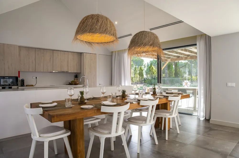 Essbereich in Villa mit großem Holztisch und zehn Stühlen, Hängeleuchten, offen zur Küche