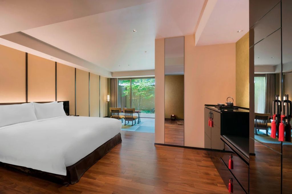 Elegantes Doppelzimmer mit Holzfußboden, großem Bett und Blick auf einen privaten Garten.