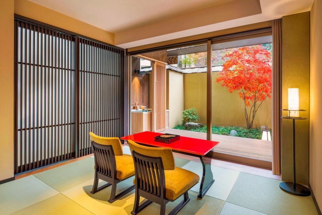 Traditionelles japanisches Teezimmer mit roten Tisch und zwei Sesseln vor einem Ahornbaum.