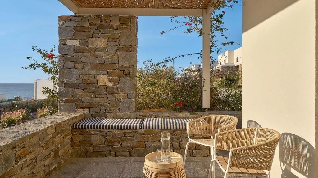 Terrasse mit Steinmauer, Sitzbank und Korbstühlen unter freiem Himmel