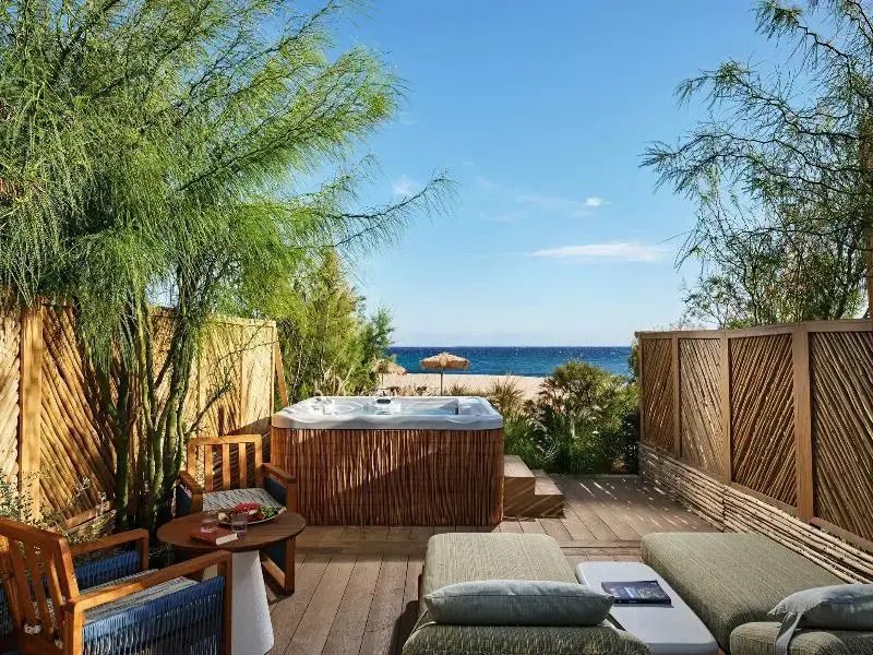 Private Terrasse mit Whirlpool und Meerblick umgeben von grünen Bäumen.