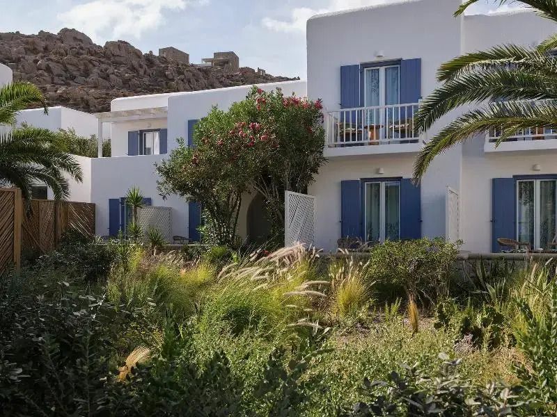 Weiße Gebäudefassade mit blauen Fensterläden umgeben von üppigem Garten