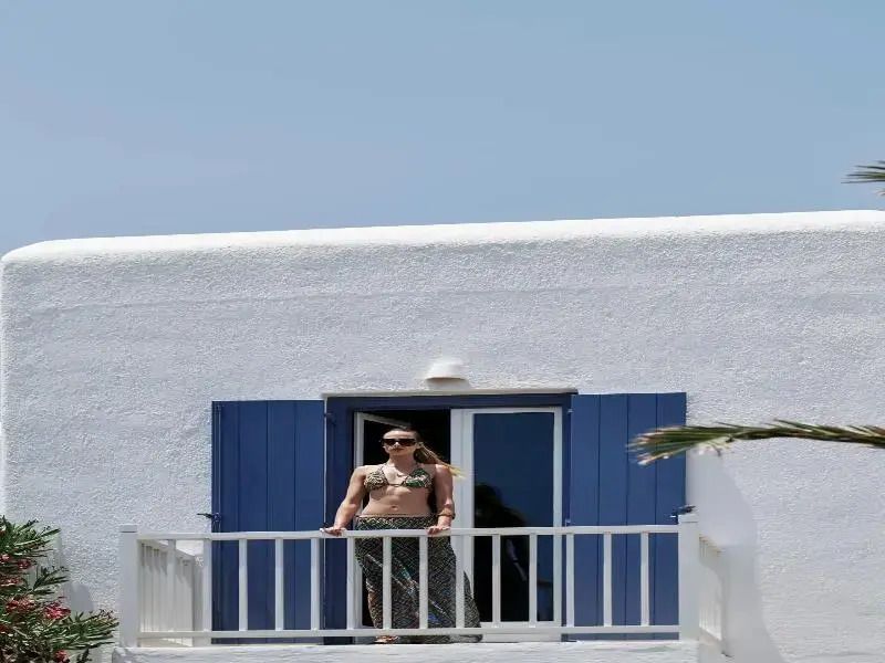 Frau auf einem Balkon einer weißen Suite mit blauen Fensterläden und Meerblick