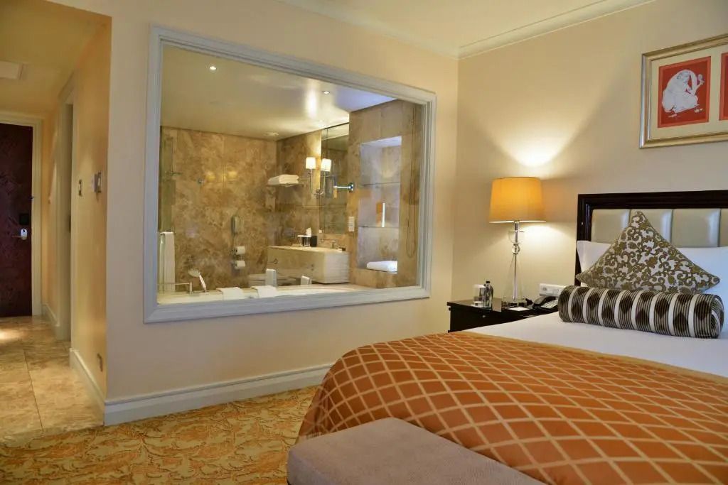 Helles Hotelzimmer mit Blick ins elegante Badezimmer durch große Fensterwand.