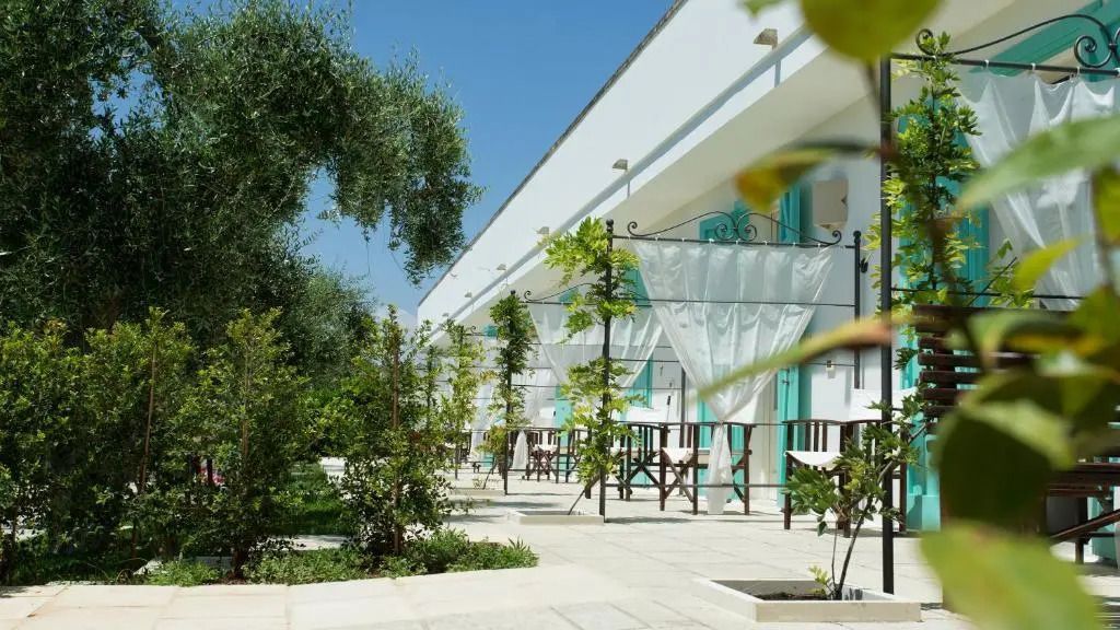 Terrasse mit grünen Pflanzen und elegantem Vorhang. Weiße Wände und türkisfarbene Fensterläden.