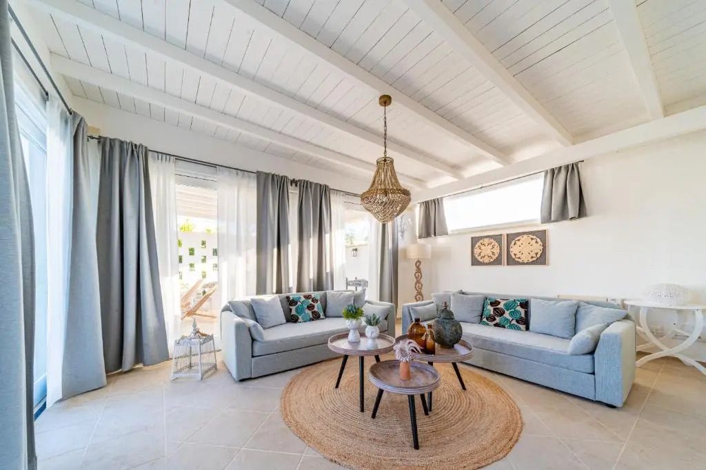 Heller Wohnbereich mit Holzdecke, grauen Sofas, kunstvoller Beleuchtung und Couchtischen
