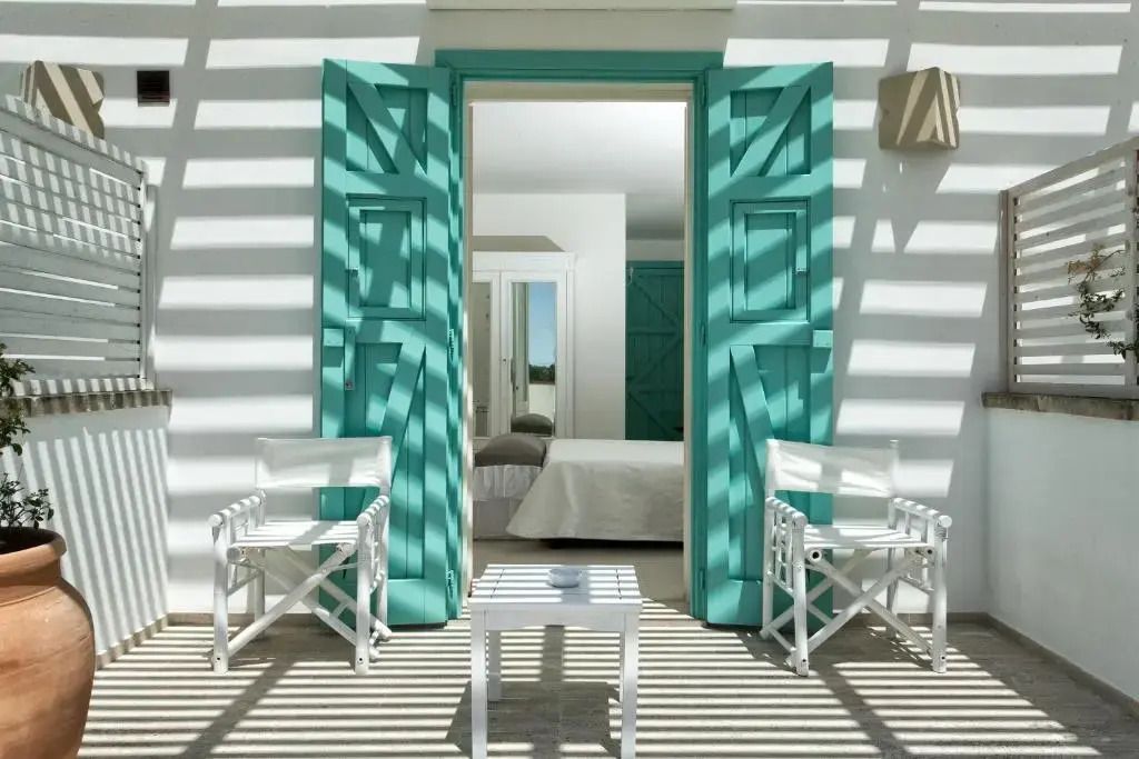 Terrasse mit türkisfarbenen Türen und stilvollen weißen Stühlen im Hotel Tenuta Centoporte.