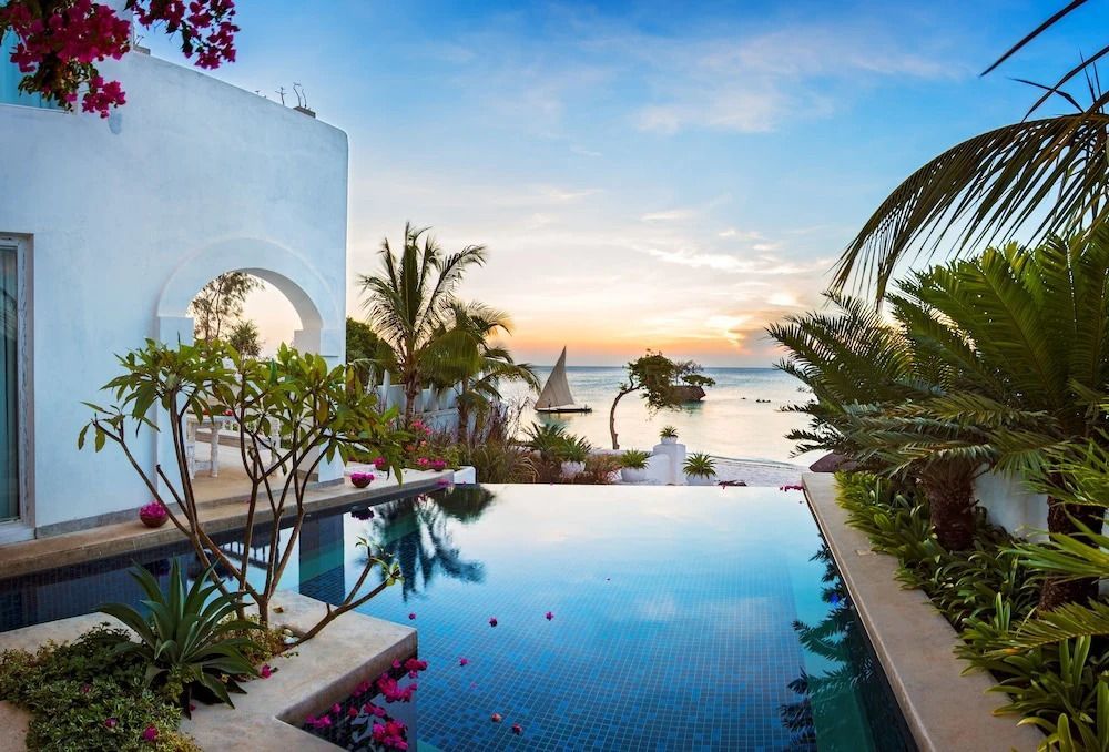 Infinity-Pool mit Blick auf Ozean und Segelboot bei Sonnenuntergang